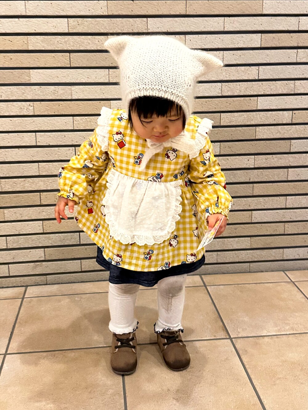 イエロー系のチュニック、ブラウン系のシューズ、ベージュ系のムートンコートを着用したキッズの冬コーディネートの2枚目の写真