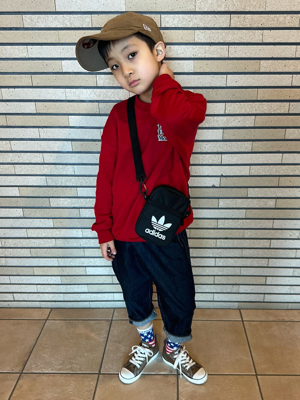 レッド系のスウェット、ブラック系のショルダーバッグ、ブルー系のデニムパンツを着用したキッズの春コーディネートの2枚目の写真