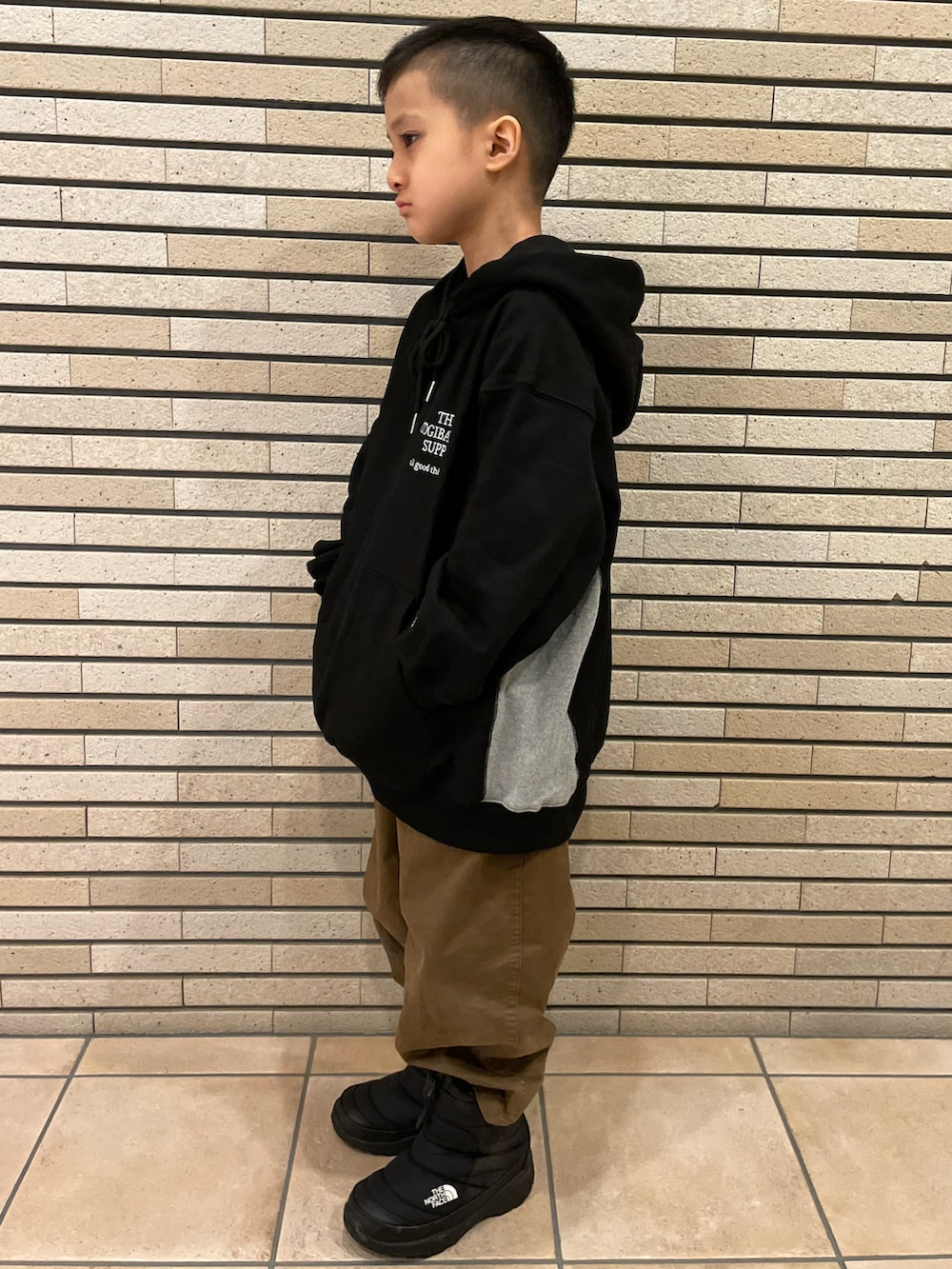 グリーン系のダウンジャケット/コート、ブラック系のパーカー、ブラウン系のチノパンツを着用したキッズの冬コーディネートの2枚目の写真