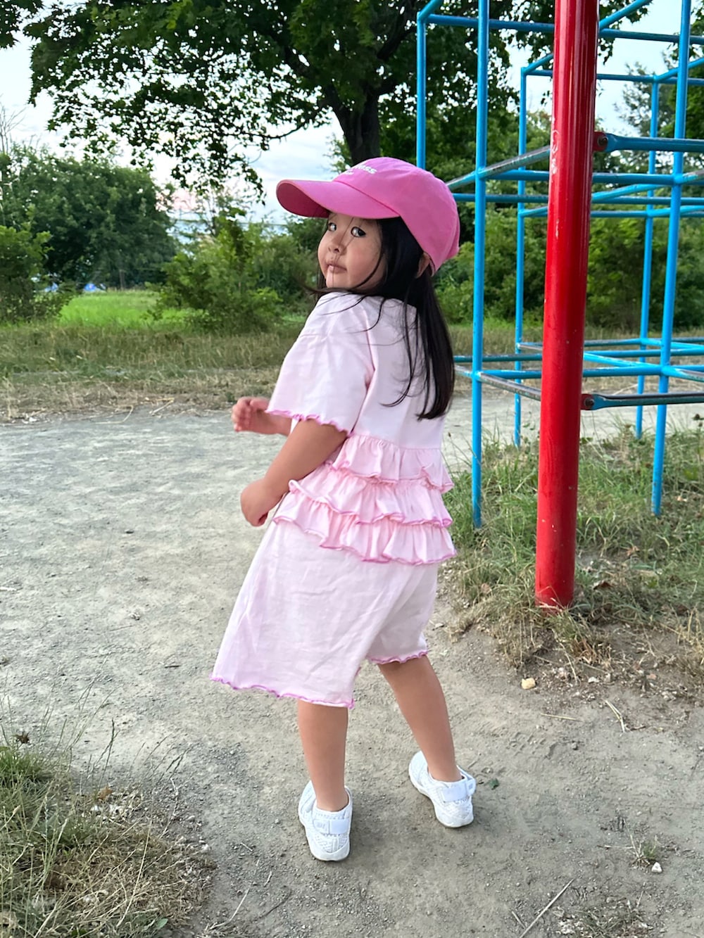 ピンク系のワンピース、ホワイト系のスニーカー、ピンク系のキャップを着用したキッズの夏コーディネートの3枚目の写真