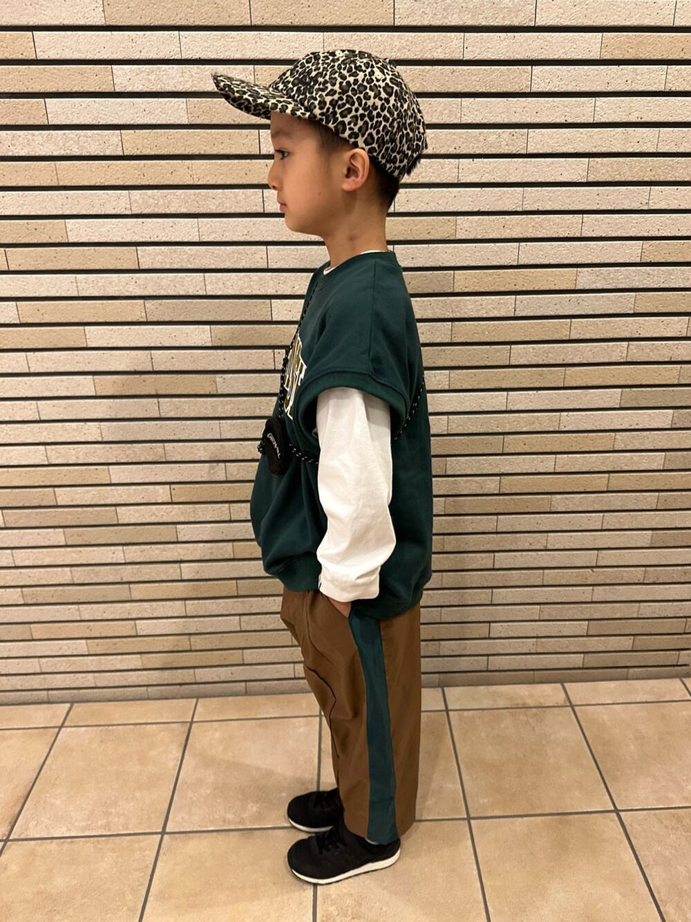 グリーン系のベスト、ホワイト系のTシャツ/カットソー、ブラウン系のパンツを着用したキッズの秋コーディネートの2枚目の写真