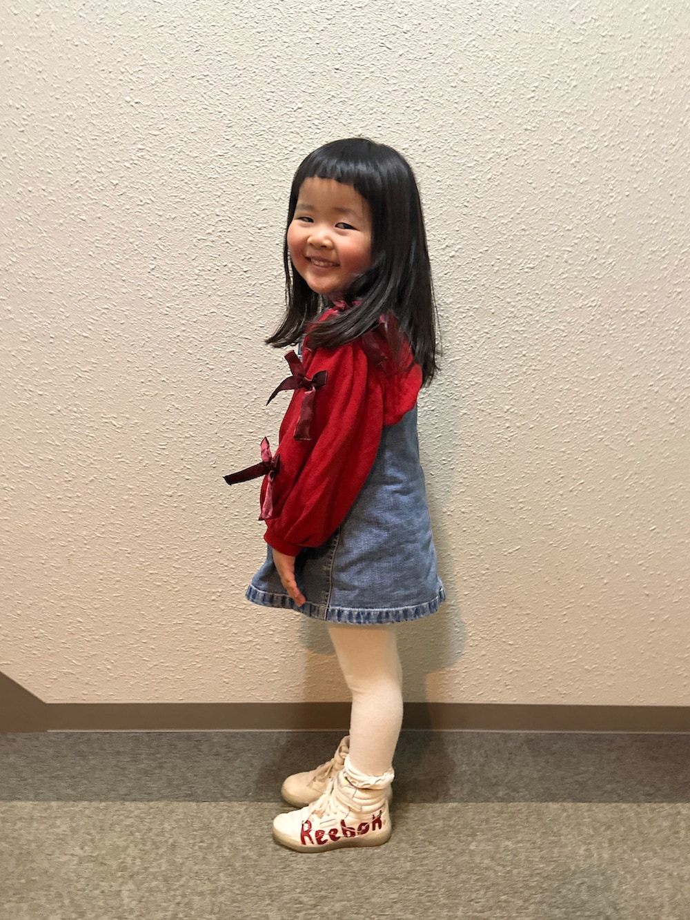 レッド系のスウェット、ブルー系のジャンパースカート、レッド系のスニーカーを着用したキッズの春コーディネートの2枚目の写真