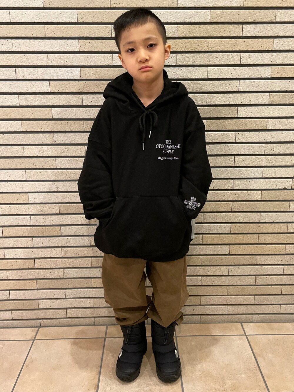グリーン系のダウンジャケット/コート、ブラック系のパーカー、ブラウン系のチノパンツを着用したキッズの冬コーディネートの3枚目の写真