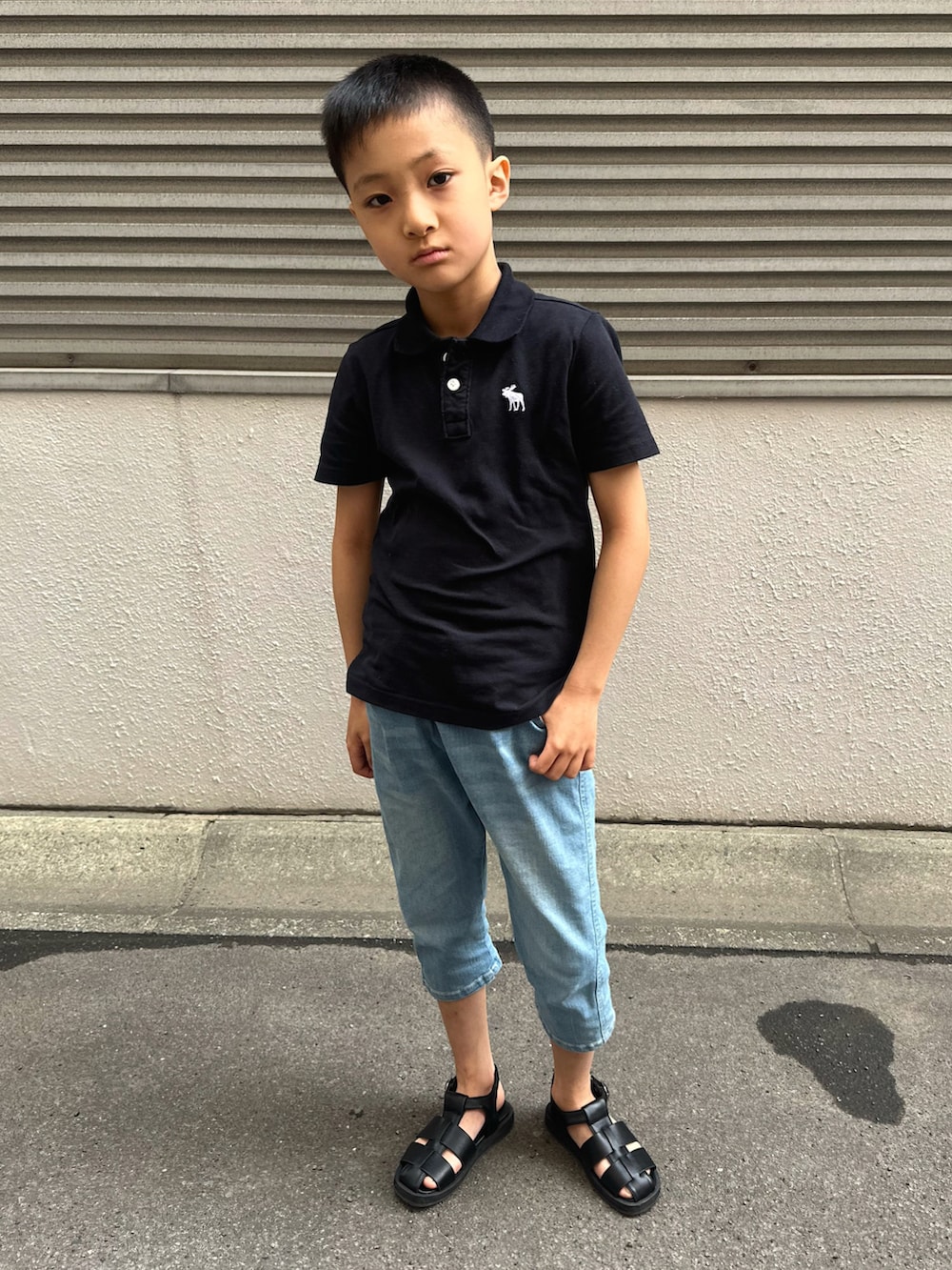 ブラック系のポロシャツ、ブルー系のデニムパンツ、ブラック系のサンダルを着用したキッズの春コーディネートの2枚目の写真