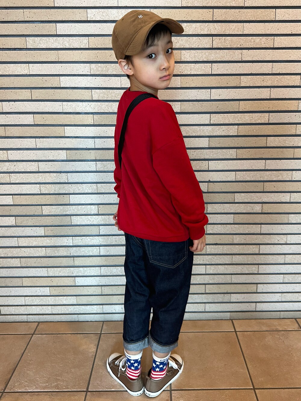 レッド系のスウェット、ブラック系のショルダーバッグ、ブルー系のデニムパンツを着用したキッズの春コーディネートの3枚目の写真