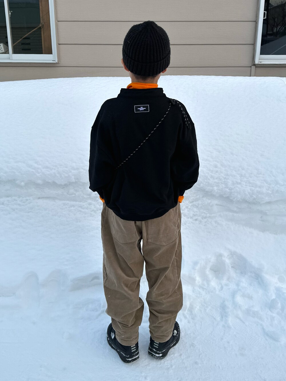 ブラック系のスウェット、オレンジ系のTシャツ/カットソー、ベージュ系のパンツを着用したキッズの春コーディネートの3枚目の写真