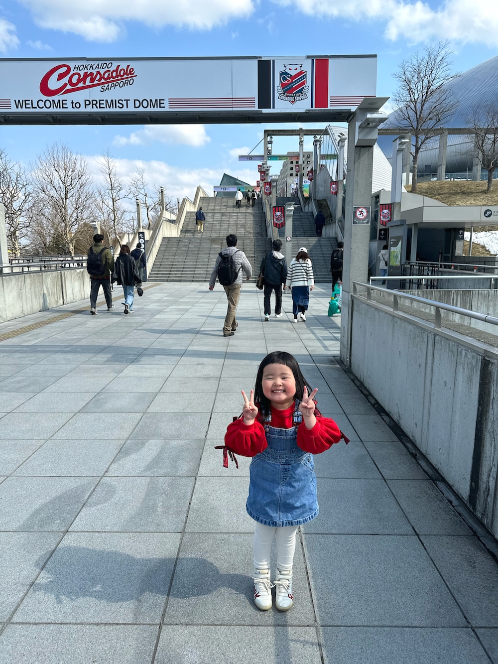 レッド系のスウェット、ブルー系のジャンパースカート、レッド系のスニーカーを着用したキッズの春コーディネートの4枚目の写真