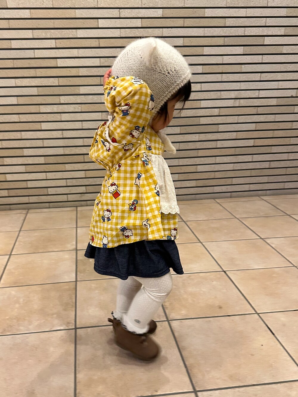 イエロー系のチュニック、ブラウン系のシューズ、ベージュ系のムートンコートを着用したキッズの冬コーディネートの3枚目の写真