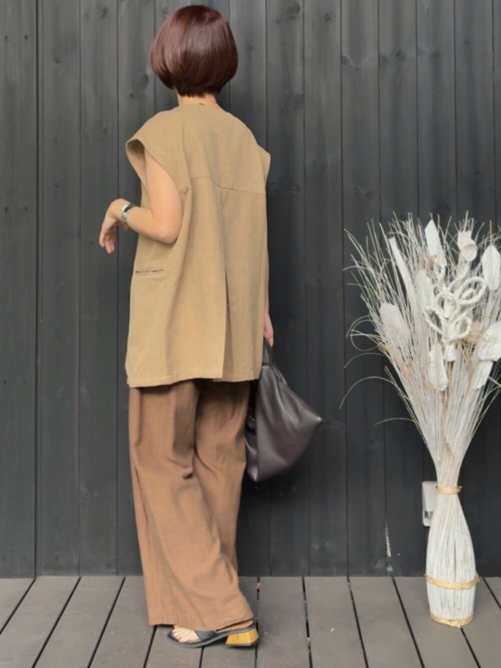 グリーン系のベスト、ブラウン系のパンツ、ブラック系のサンダルを着用したレディースの春コーディネートの2枚目の写真