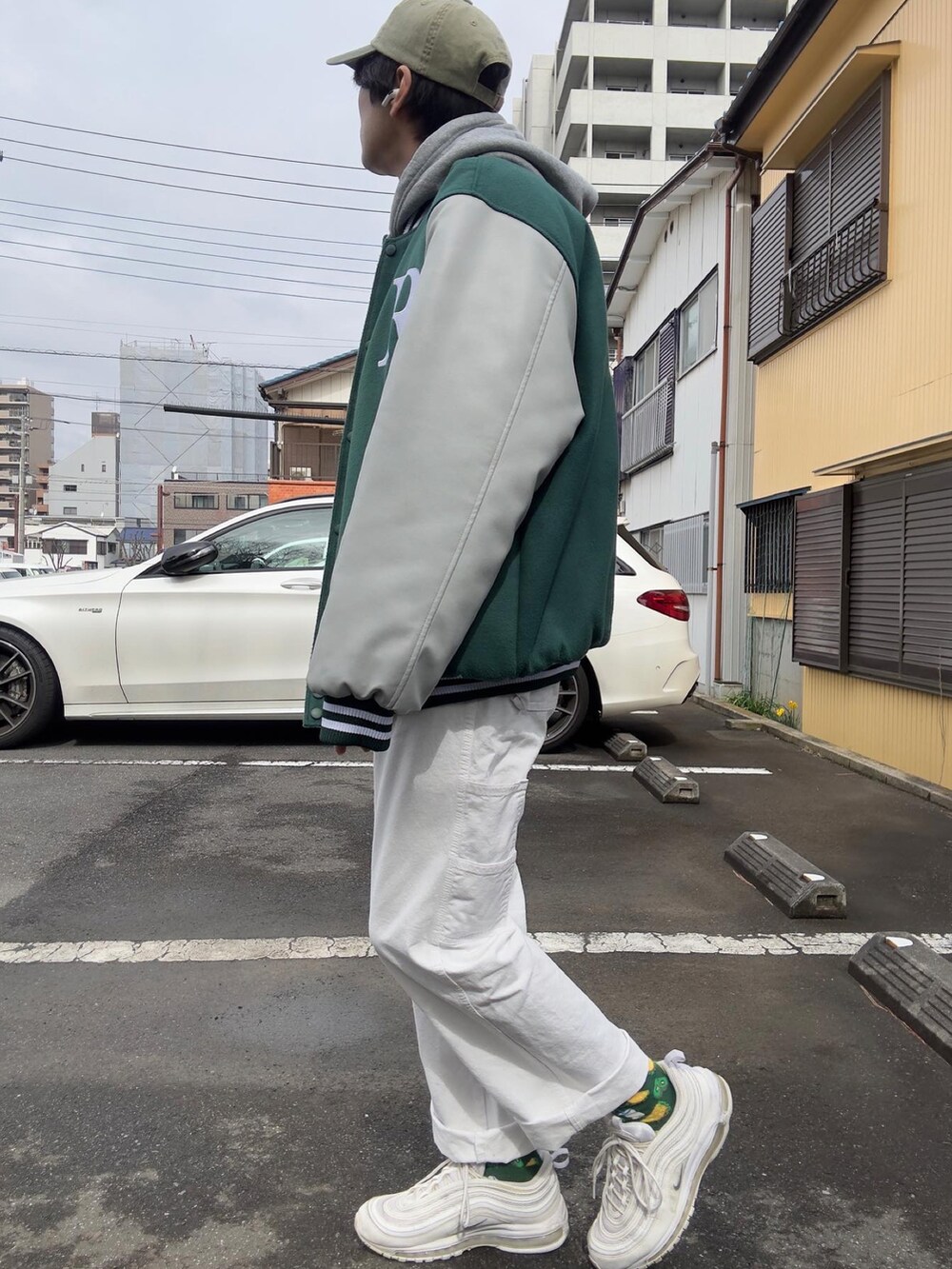 グリーン系のスタジャン、グレー系のパーカー、ホワイト系のカーゴパンツを着用したメンズの春コーディネートの2枚目の写真