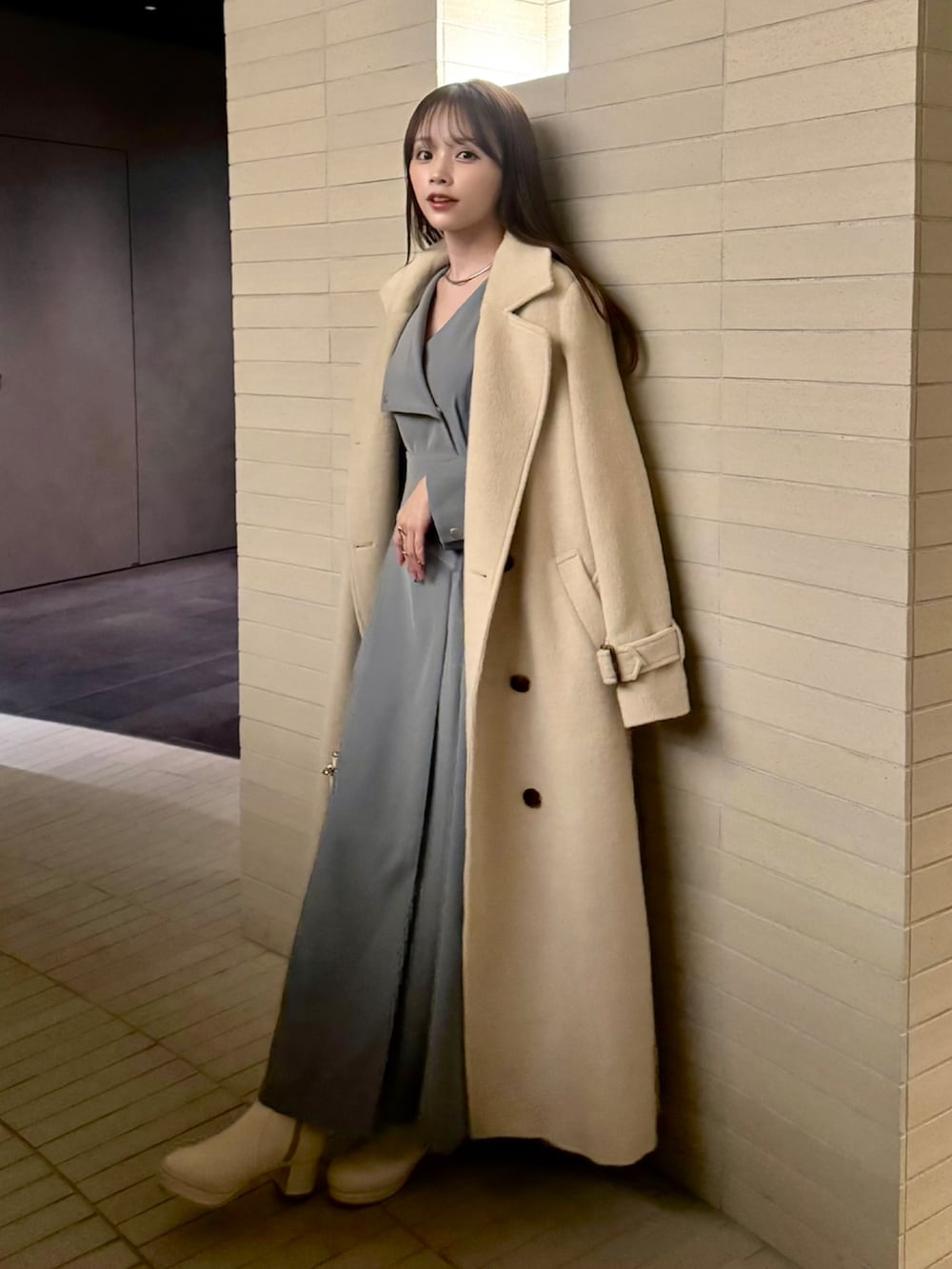 グレー系のワンピース、ホワイト系のステンカラーコート、ホワイト系のブーツを着用したレディースの冬コーディネートの2枚目の写真