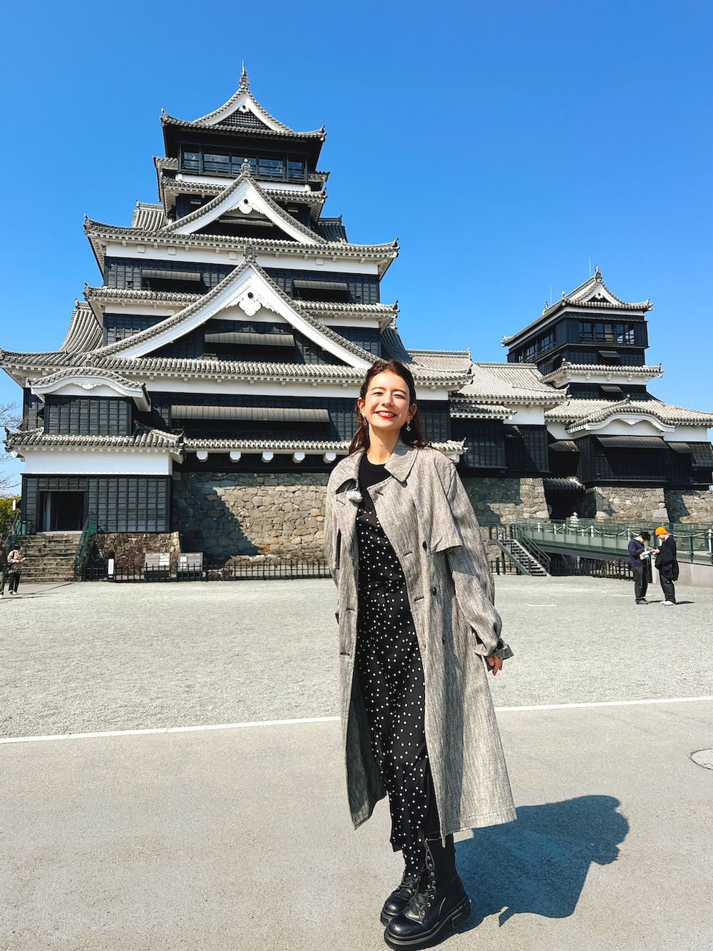 ブラック系のブーツ、グレー系のトレンチコート、ブラック系のドレスを着用したレディースの春コーディネートの2枚目の写真