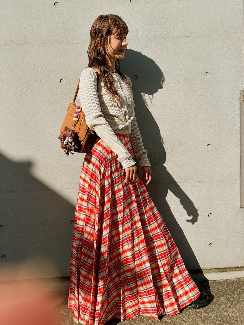 レッド系のスカート、ベージュ系のカーディガン/ボレロ、ブラウン系のバッグを着用したレディースの秋コーディネートの2枚目の写真