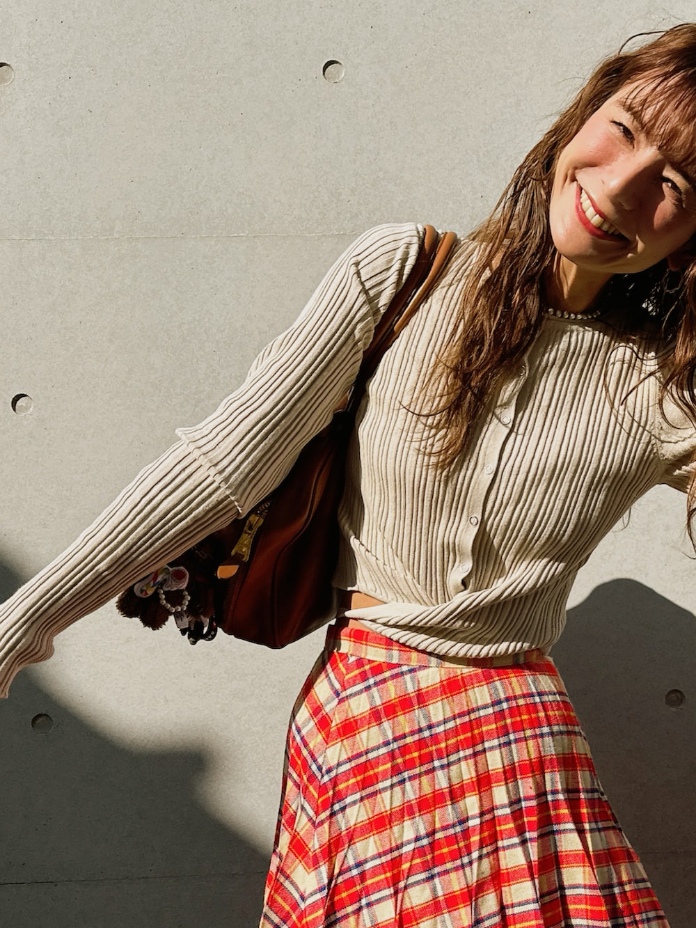 レッド系のスカート、ベージュ系のカーディガン/ボレロ、ブラウン系のバッグを着用したレディースの秋コーディネートの3枚目の写真