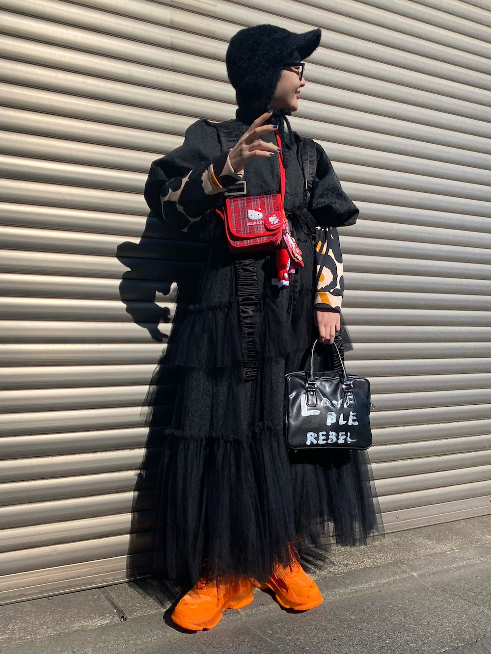 オレンジ系のスニーカー、ブラック系のベスト、ブラック系のバッグを着用したレディースの春コーディネートの2枚目の写真