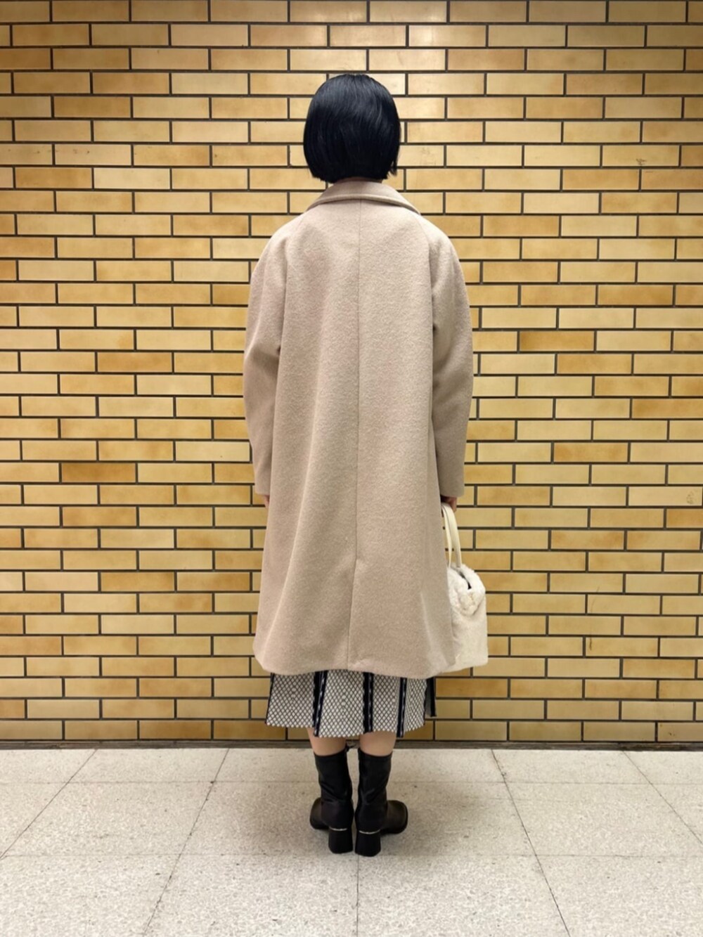 ブラック系のブーツ、ベージュ系のステンカラーコート、ブルー系のワンピースを着用したレディースの冬コーディネートの3枚目の写真