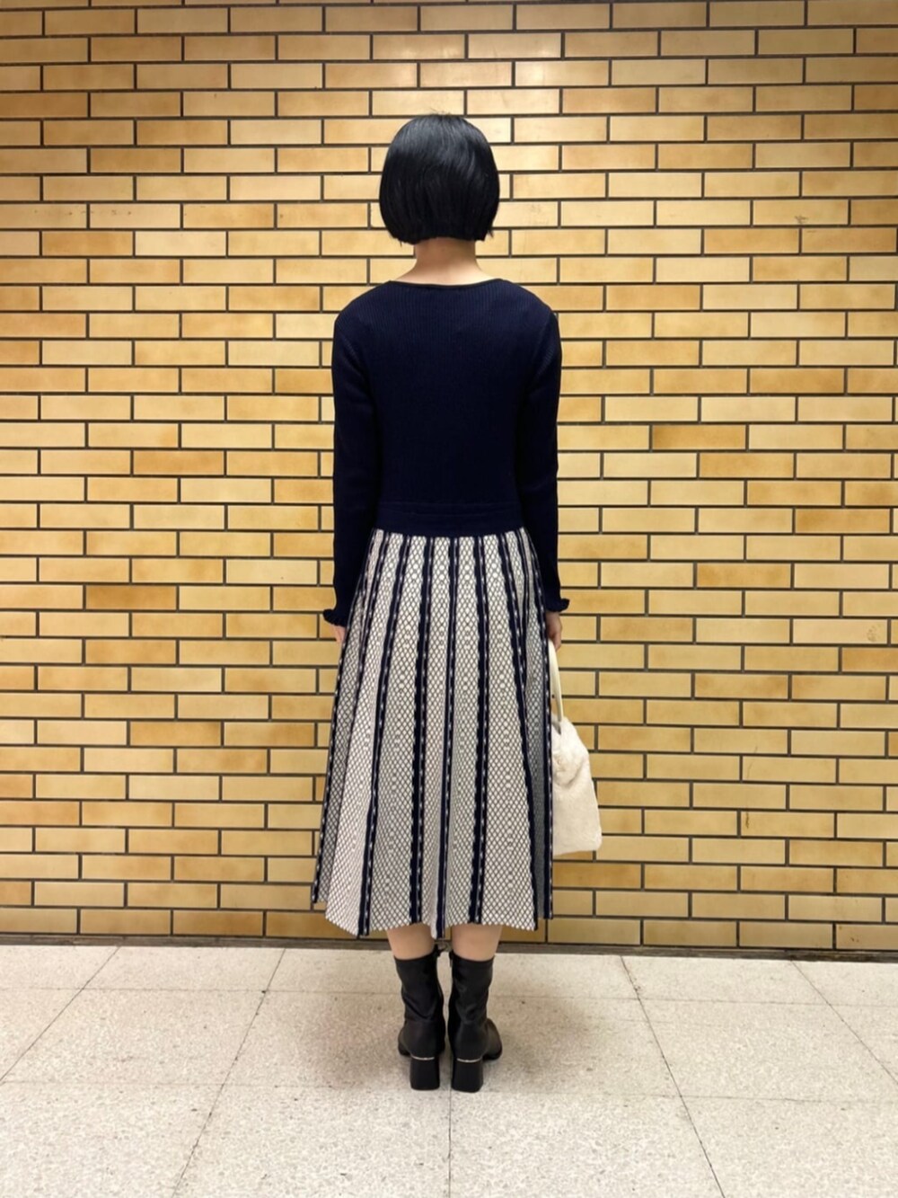 ブラック系のブーツ、ブルー系のワンピース、ホワイト系のハンドバッグを着用したレディースの冬コーディネートの3枚目の写真