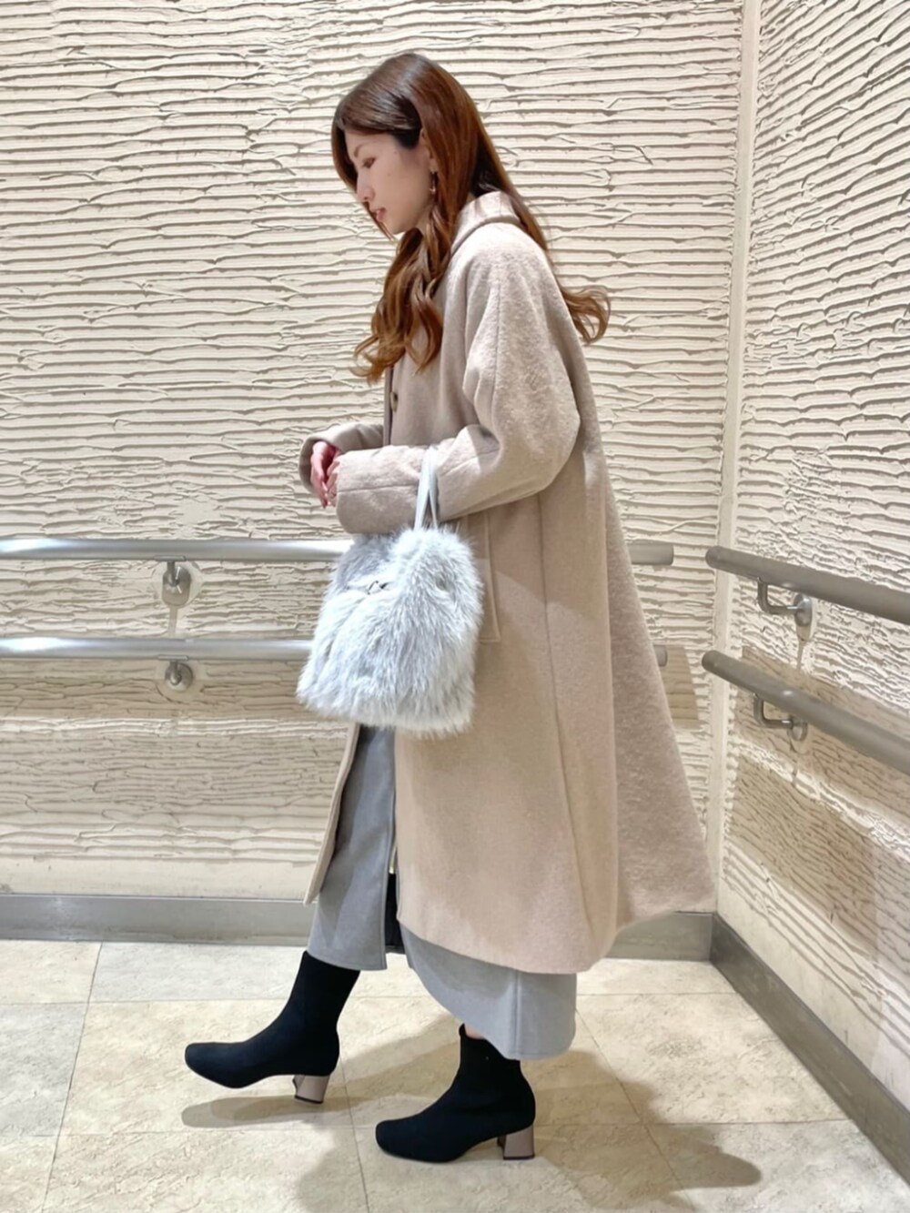 ブラック系のブーツ、グレー系のスカート、ベージュ系のステンカラーコートを着用したレディースの冬コーディネートの2枚目の写真