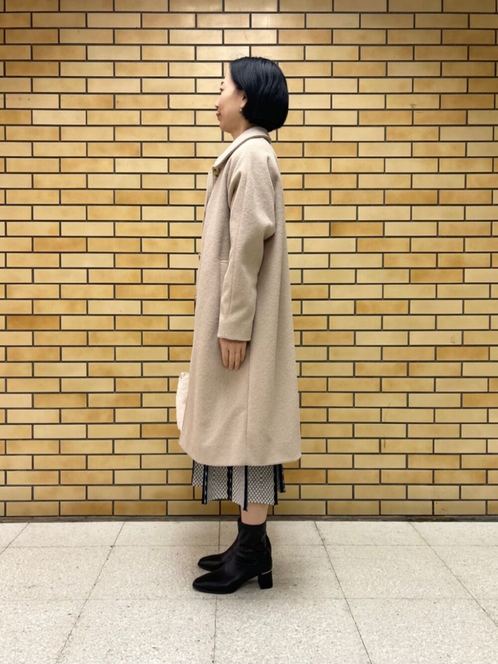 ブラック系のブーツ、ベージュ系のステンカラーコート、ブルー系のワンピースを着用したレディースの冬コーディネートの2枚目の写真