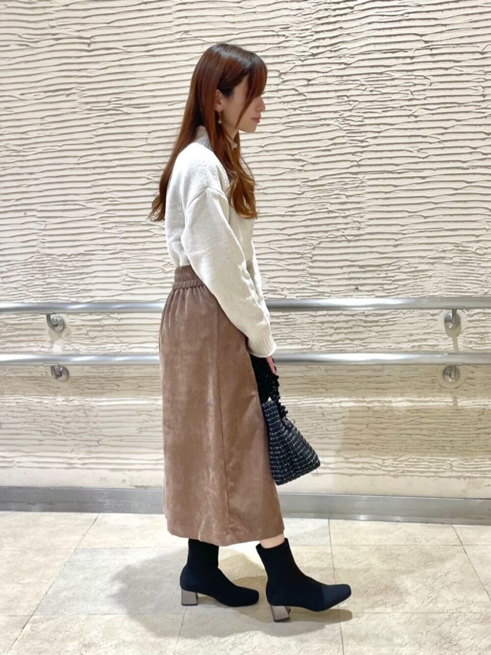 ブラック系のブーツ、ホワイト系のニット/セーター、ブラウン系のスカートを着用したレディースの冬コーディネートの2枚目の写真
