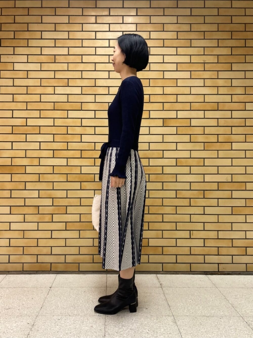 ブラック系のブーツ、ブルー系のワンピース、ホワイト系のハンドバッグを着用したレディースの冬コーディネートの2枚目の写真