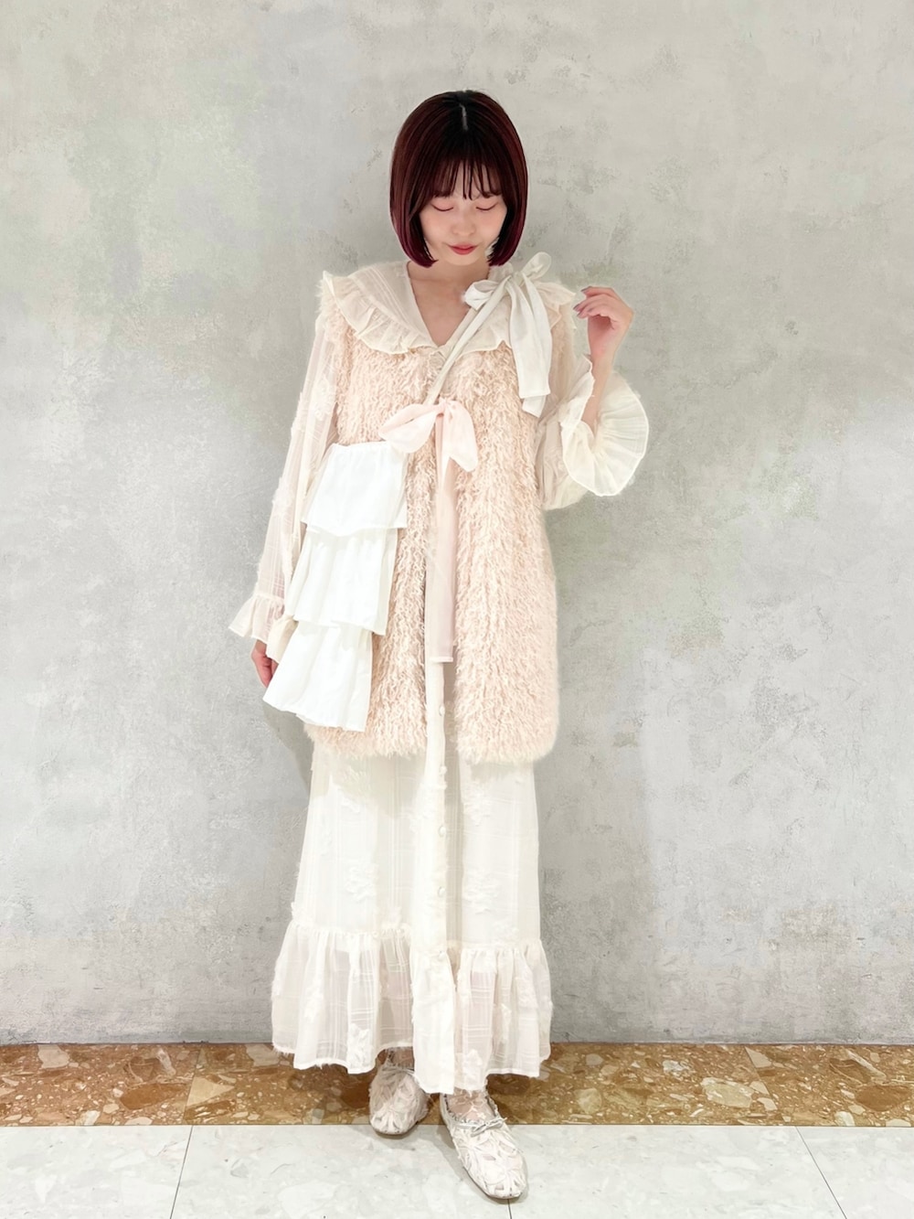 ホワイト系のダウンベスト、グリーン系のパンプス、ホワイト系のワンピースを着用したレディースの冬コーディネートの2枚目の写真