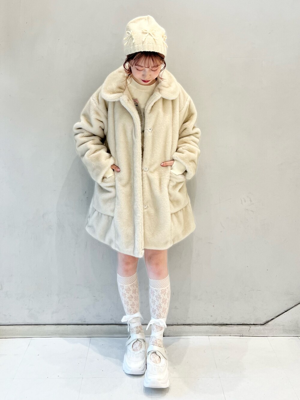 ホワイト系のノーカラーコート、ホワイト系のスカート、ホワイト系のニット/セーターを着用したレディースの冬コーディネートの3枚目の写真