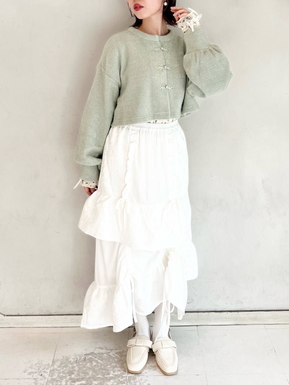 グリーン系のカーディガン/ボレロ、ホワイト系のスカート、ホワイト系のTシャツ/カットソーを着用したレディースの秋コーディネートの3枚目の写真