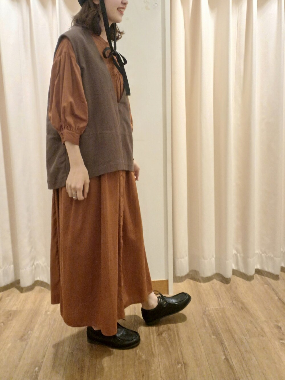 ブラウン系のベスト、オレンジ系のワンピース、ブラック系のその他シューズを着用したレディースの秋コーディネートの2枚目の写真