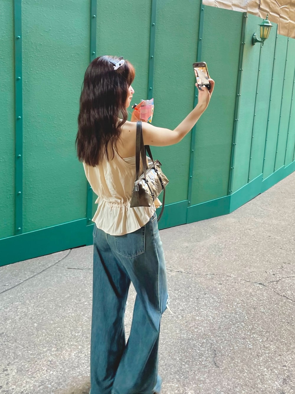 ブラウン系のショルダーバッグ、グリーン系のスニーカー、ブルー系のデニムパンツを着用したレディースの秋コーディネートの2枚目の写真