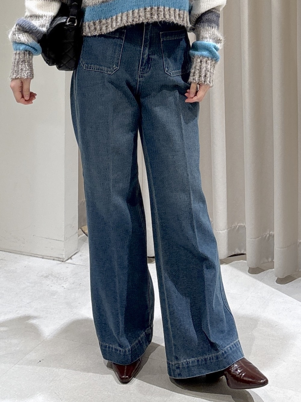 グレー系のニット/セーター、ブラック系のショルダーバッグ、ブルー系のデニムパンツを着用したレディースの秋コーディネートの5枚目の写真