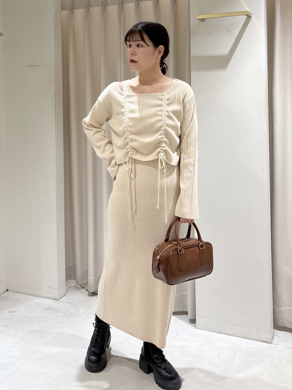 ホワイト系のワンピース、ブラウン系のハンドバッグ、ブラック系のブーツを着用したレディースの冬コーディネートの2枚目の写真