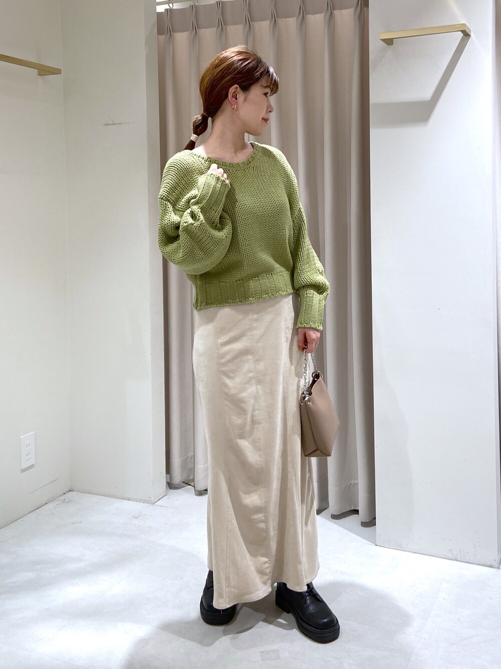 グリーン系のニット/セーター、ホワイト系のスカート、ベージュ系のショルダーバッグを着用したレディースの秋コーディネートの3枚目の写真