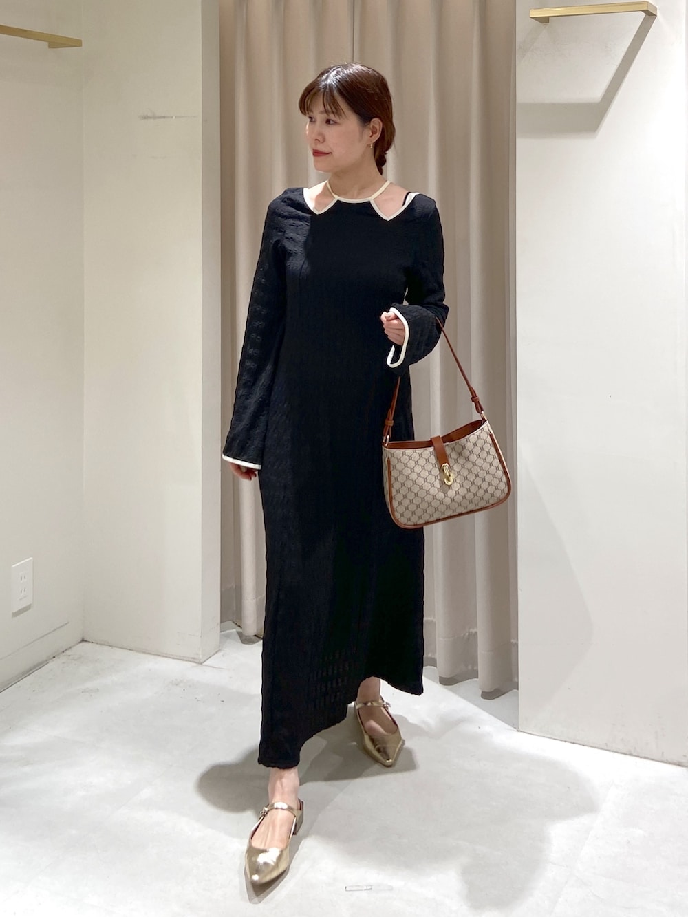 ブラック系のワンピース、ベージュ系のショルダーバッグ、ゴールド系のパンプスを着用したレディースの春コーディネートの2枚目の写真