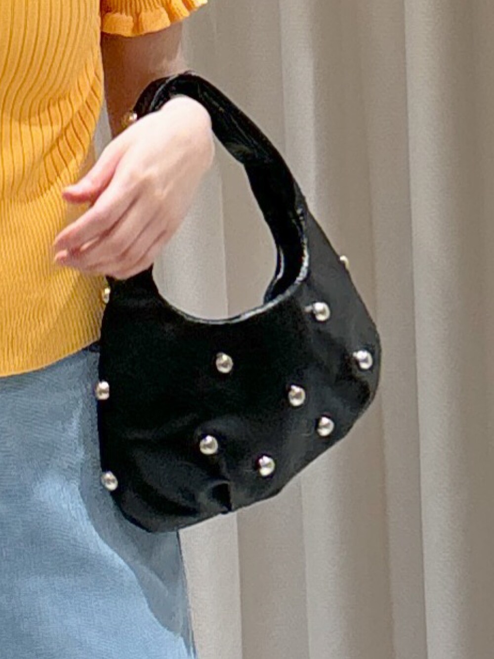 オレンジ系のニット/セーター、ブラック系のハンドバッグ、ブルー系のデニムパンツを着用したレディースの夏コーディネートの6枚目の写真