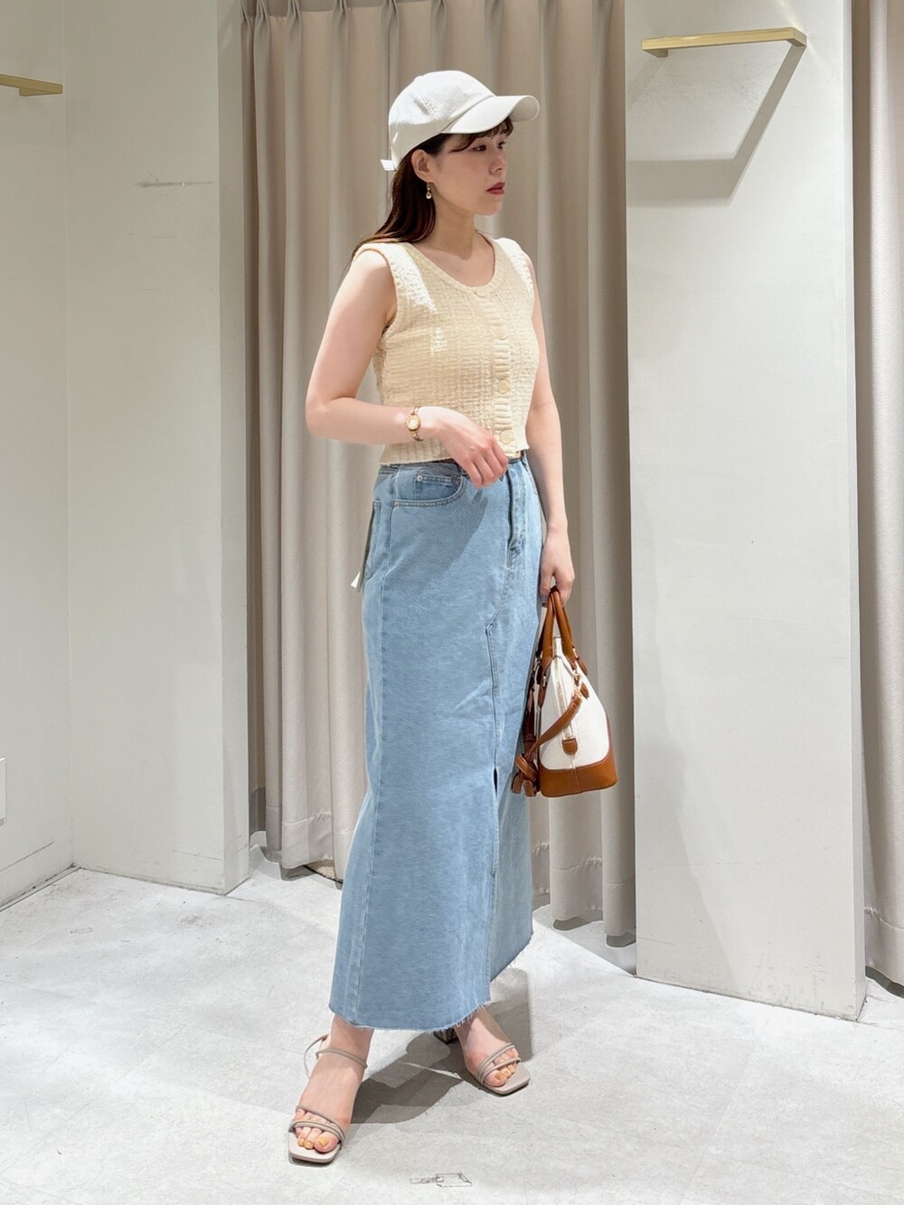 ホワイト系のベスト、ブルー系のデニムスカート、グレー系のサンダルを着用したレディースの春コーディネートの4枚目の写真
