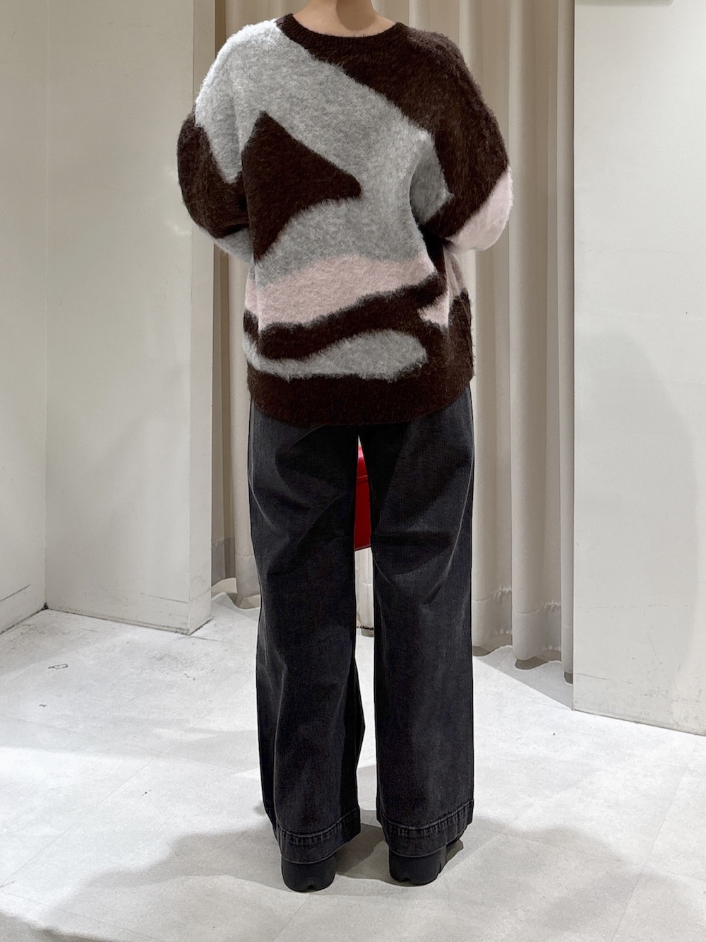 ブラウン系のニット/セーター、レッド系のハンドバッグ、ブラック系のデニムパンツを着用したレディースの秋コーディネートの3枚目の写真