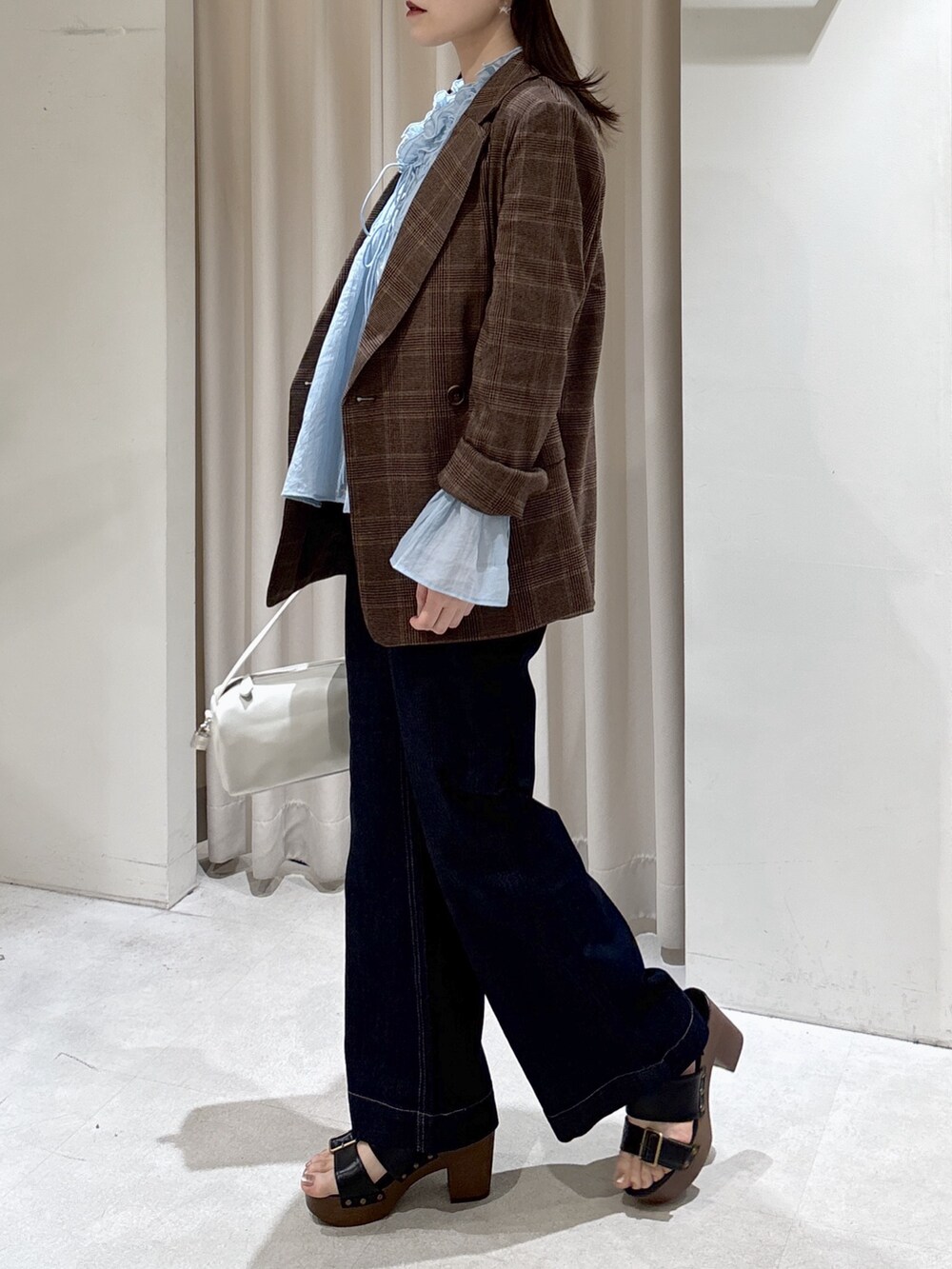 ブラウン系のテーラードジャケット、ホワイト系のハンドバッグ、ブルー系のデニムパンツを着用したレディースの春コーディネートの5枚目の写真