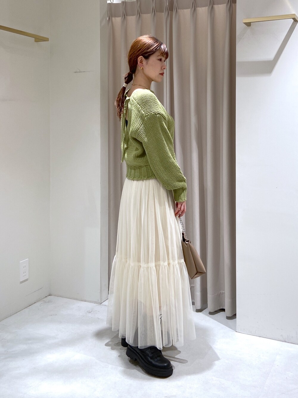 グリーン系のニット/セーター、ホワイト系のスカート、ベージュ系のショルダーバッグを着用したレディースの秋コーディネートの3枚目の写真