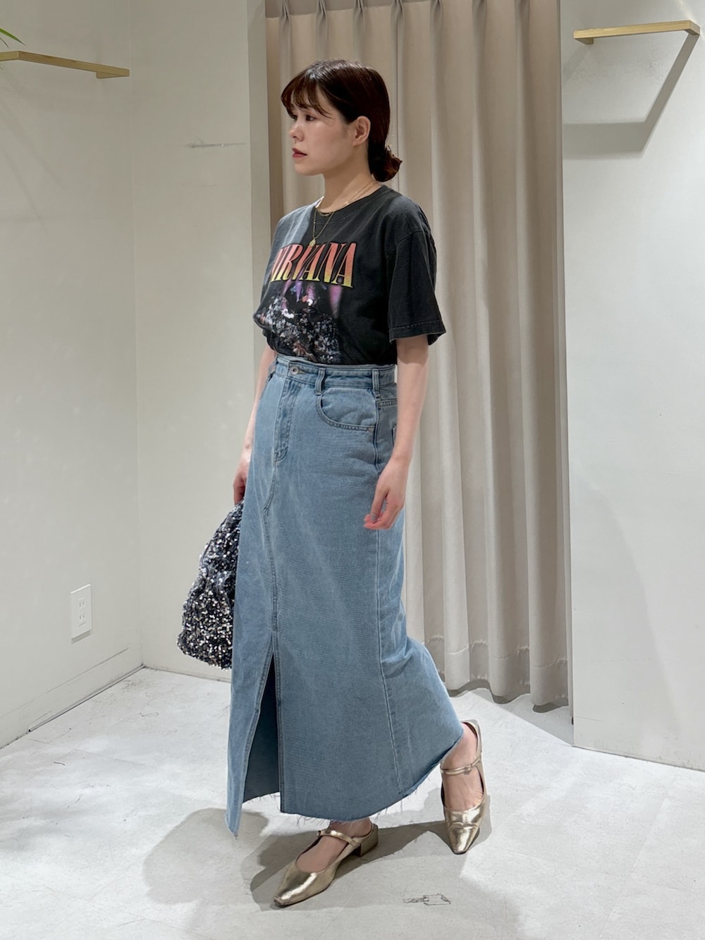 ブルー系のデニムスカート、ゴールド系のパンプス、ブラック系のTシャツ/カットソーを着用したレディースの春コーディネートの2枚目の写真