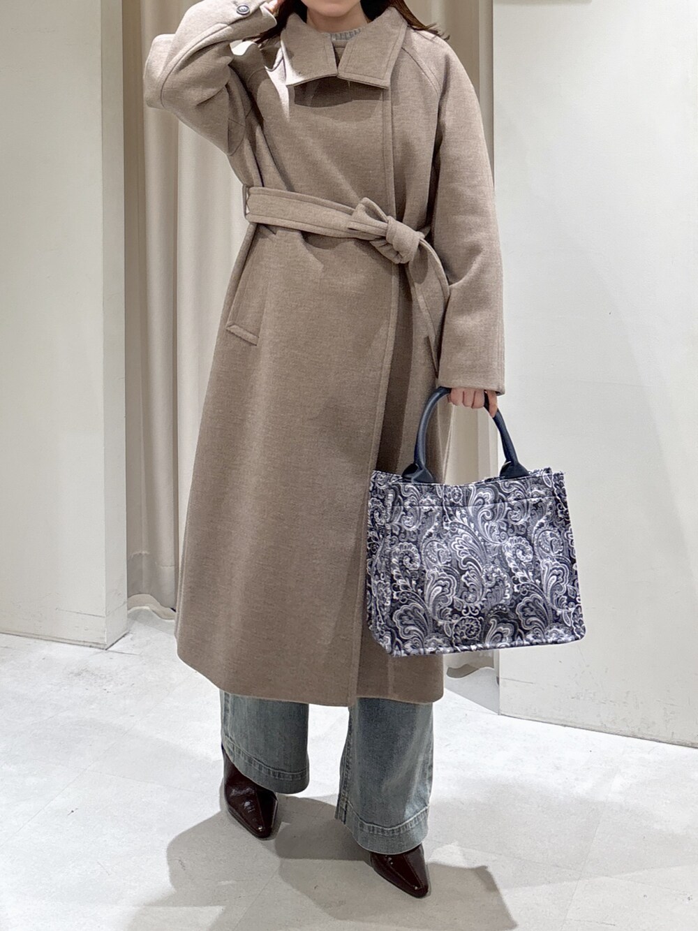 ブラウン系のステンカラーコート、ブルー系のトートバッグ、ブルー系のデニムパンツを着用したレディースの秋コーディネートの2枚目の写真