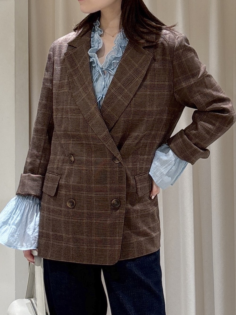 ブラウン系のテーラードジャケット、ホワイト系のハンドバッグ、ブルー系のデニムパンツを着用したレディースの春コーディネートの6枚目の写真