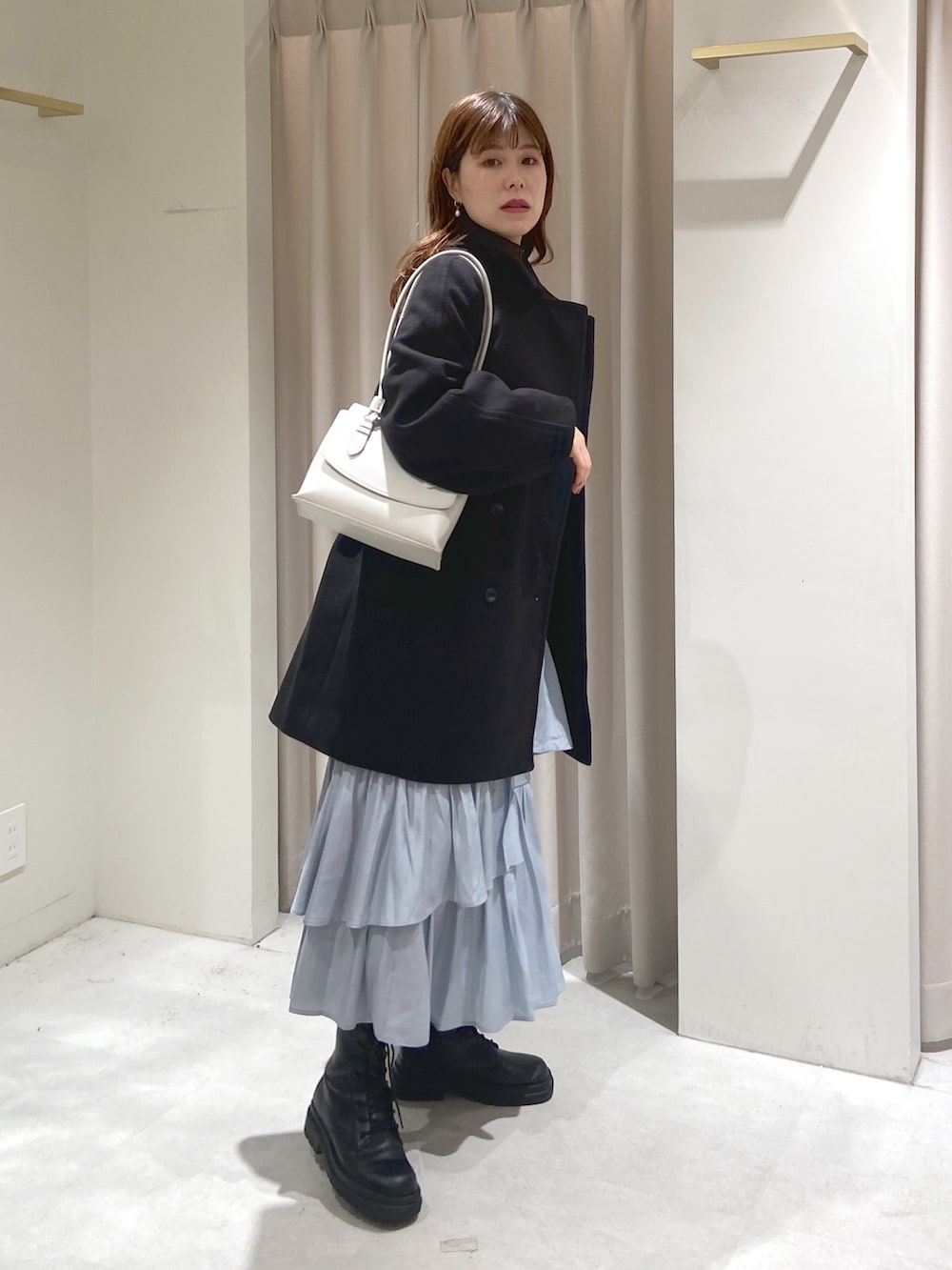 ブラック系のステンカラーコート、ホワイト系のショルダーバッグ、グレー系のスカートを着用したレディースの冬コーディネートの2枚目の写真