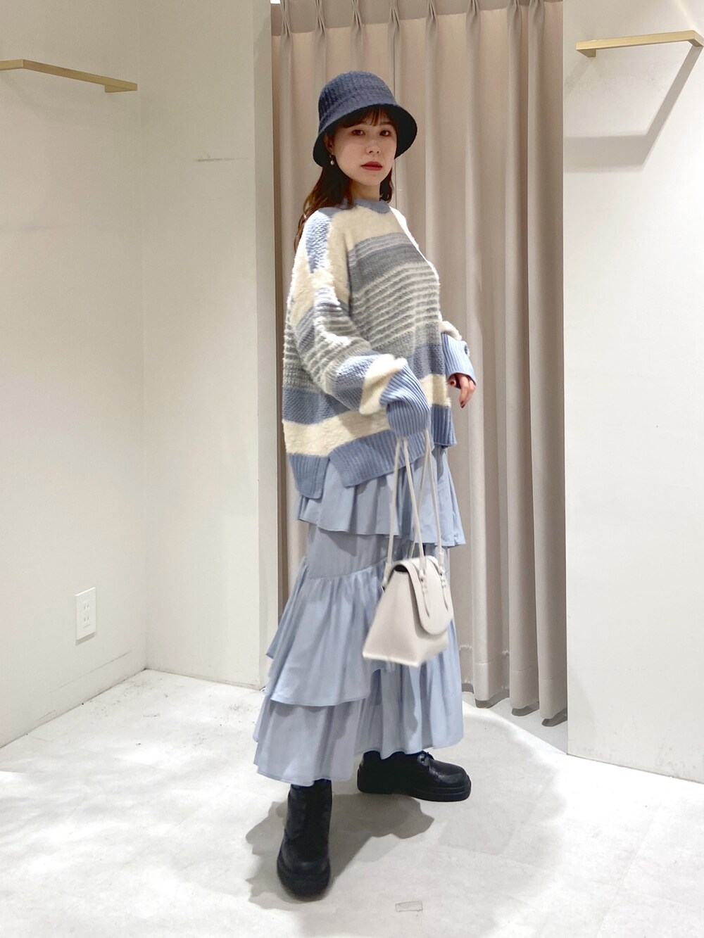 ブルー系のニット/セーター、グレー系のスカート、ホワイト系のショルダーバッグを着用したレディースの冬コーディネートの2枚目の写真