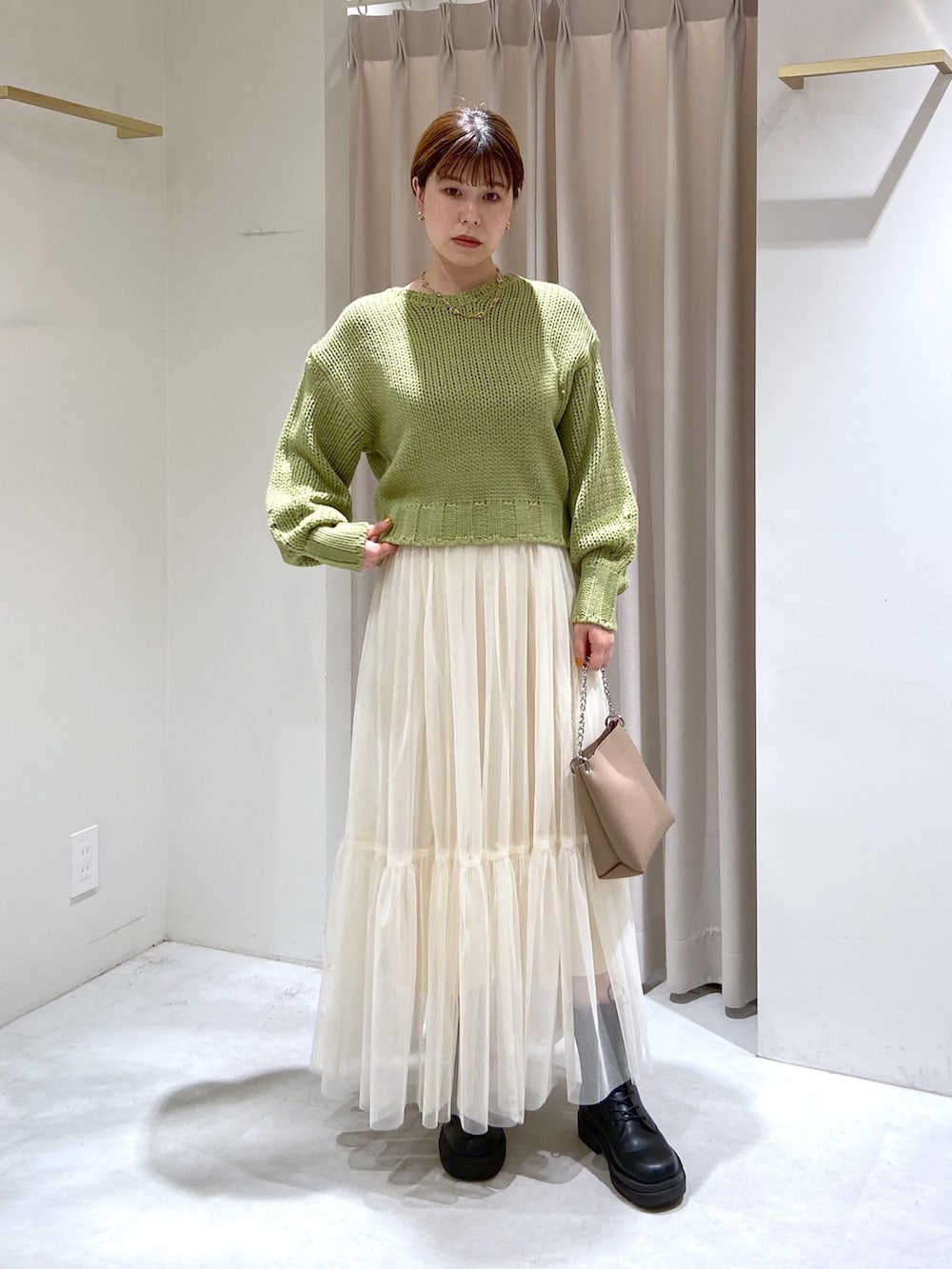 グリーン系のニット/セーター、ホワイト系のスカート、ベージュ系のショルダーバッグを着用したレディースの秋コーディネートの2枚目の写真