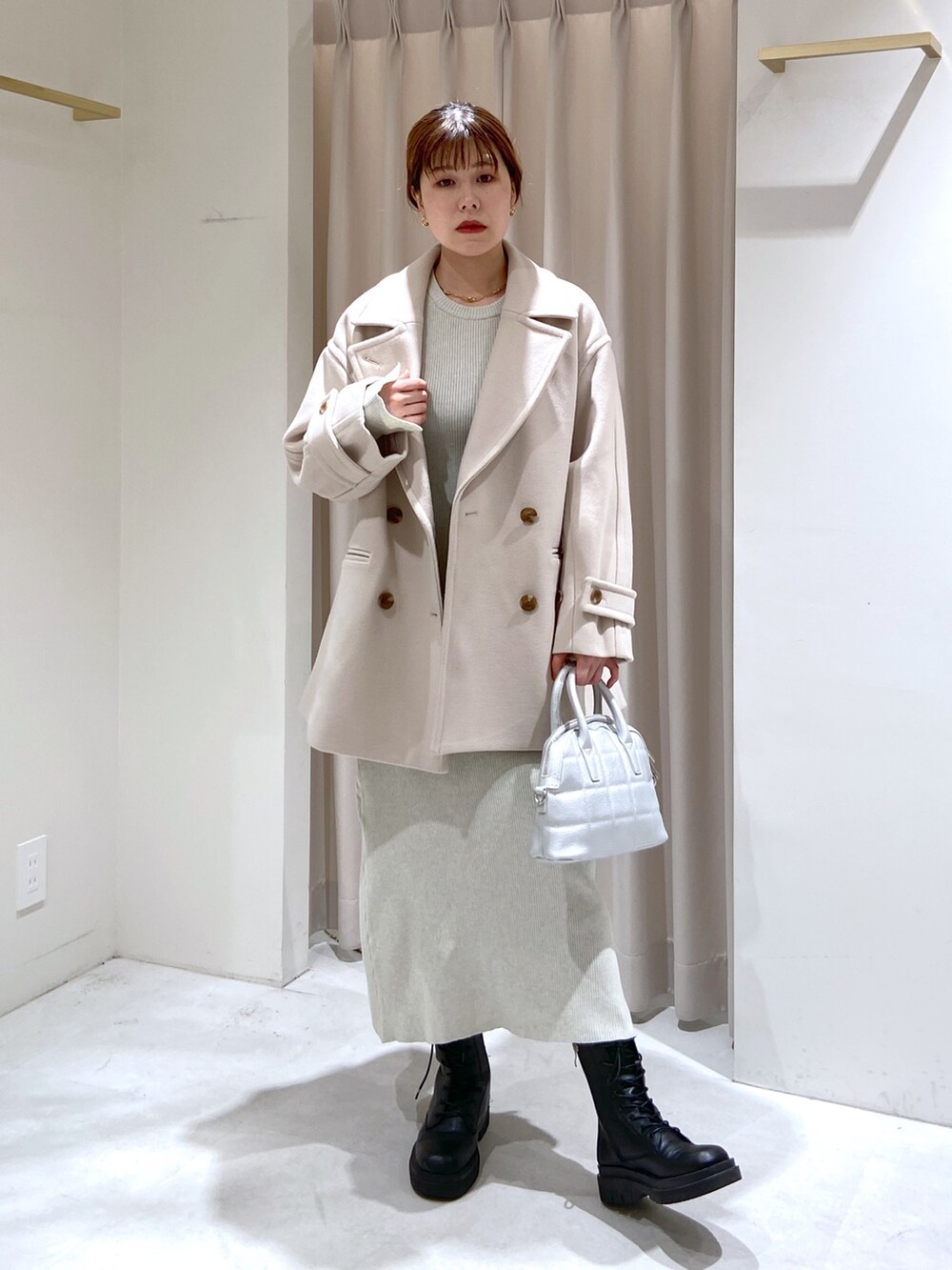 ベージュ系のピーコート、ブラック系のブーツ、シルバー系のショルダーバッグを着用したレディースの秋コーディネートの2枚目の写真