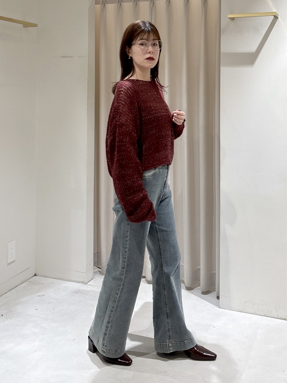 レッド系のニット/セーター、ブラウン系のトートバッグ、ブルー系のデニムパンツを着用したレディースの秋コーディネートの2枚目の写真