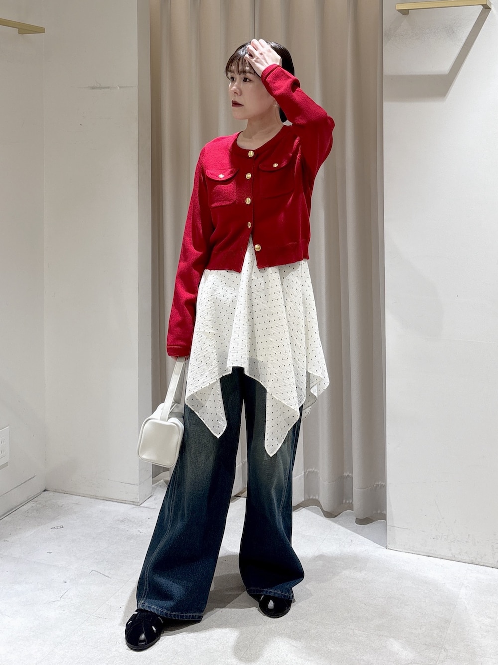 レッド系のニット/セーター、ホワイト系のワンピース、ブルー系のデニムパンツを着用したレディースの春コーディネートの6枚目の写真