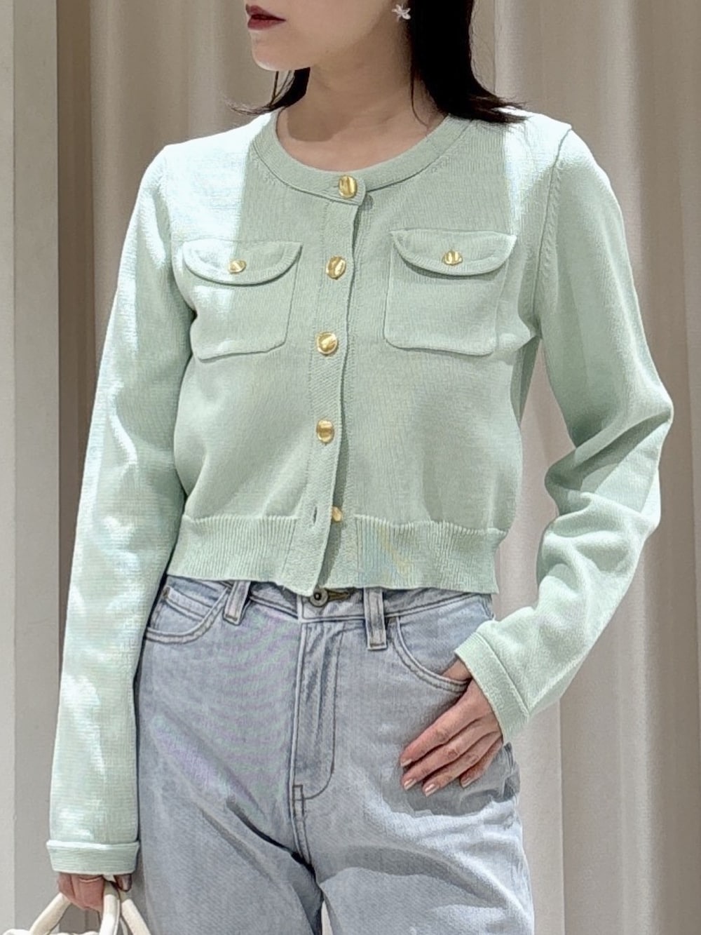 グリーン系のニット/セーター、ホワイト系のボストンバッグ、ブルー系のデニムパンツを着用したレディースの春コーディネートの2枚目の写真