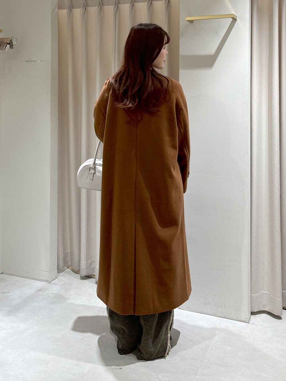 ブラウン系のチェスターコート、ブラック系のニット/セーター、ホワイト系のトートバッグを着用したレディースの秋コーディネートの4枚目の写真